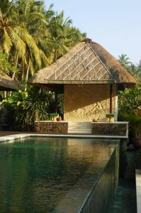 a resort with a swimming pool and a thatch roof at Villa Kanti in Ubud