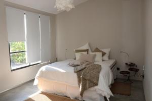 ein weißes Schlafzimmer mit einem Bett mit Kissen und einem Fenster in der Unterkunft Las Glicinas Boutique Apartments in Colonia del Sacramento