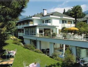 una gran casa blanca con mesas y sillas en una colina en Hotel Annabell, en Merano