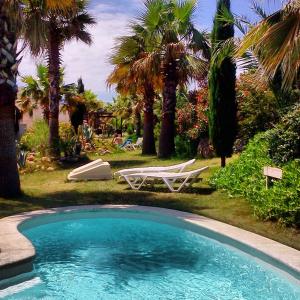 una piscina con 2 sillas de césped y palmeras en L' Escala Resort en L'Escala