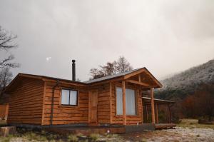 una cabaña de madera en un campo con montañas al fondo en Cabañas Tunquelen Malalcahuello, en Malalcahuello