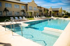 a swimming pool with white chairs and a building at Hotel Howard Johnson Trenque Lauquen in Trenque Lauquen