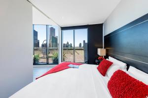 1 dormitorio con 1 cama blanca grande con almohadas rojas en Aura on Flinders Serviced Apartments, en Melbourne