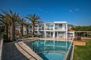 uma casa grande com piscina e palmeiras em Happy Days Beach Hotel em Georgioupolis