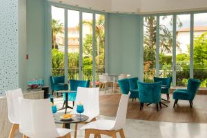 a restaurant with white chairs and tables and windows at Hôtel Miléade L'Orangeraie - Menton in Menton