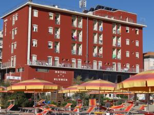 um edifício vermelho com mesas, cadeiras e guarda-sóis em Hotel Blumen em Rimini