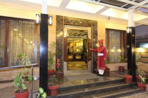 een man in een rode mantel die voor de deur van een gebouw staat bij Amantra Comfort Hotel in Udaipur