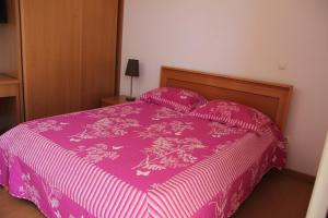 Bett mit rosa Tagesdecke und Kissen in der Unterkunft Apartamento António in Praia