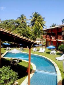 a swimming pool with chairs and umbrellas next to a resort at Pousada Thalud in Imbassai