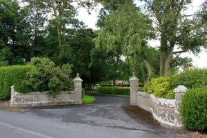 a stone fence and a driveway with bushes and trees at Garrane House in Croom
