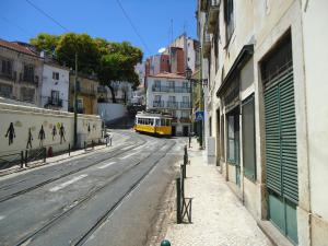 リスボンにあるAlfama 2 Youの黄色い列車が建物のある街路を走る