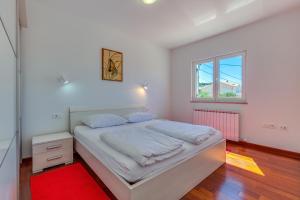 a white bedroom with a bed with a red rug at Apartments Host in Rab