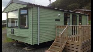 a green tiny house with a wooden porch at Seaview caravans in Aberystwyth