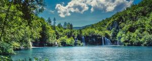 a lake with a waterfall in the middle of a forest at Guest House Olbina in Korenica