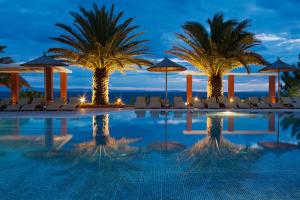 a pool with chairs and palm trees at night at Alexandra Beach Spa Resort in Potos