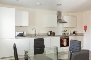 eine Küche mit weißen Schränken und einem Glastisch in der Unterkunft House of Fisher- Solstice House Apartments in Farnborough