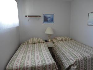 two twin beds in a bedroom with a lamp and a window at Bella Villa Resort Motel in Osoyoos