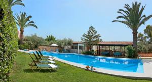 a large swimming pool with lounge chairs and palm trees at Argo Apartments in Kato Daratso