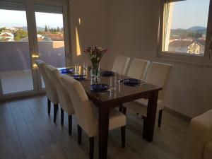 a dining room table with white chairs and a table with a view at Apartman Lora in Ljubuški