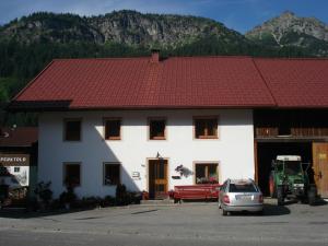 a white building with a red roof with a car parked in front at Haus Walter in Nesselwängle