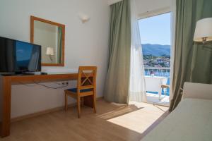 um quarto com uma secretária, uma televisão e uma janela em Hotel Saron em Poros