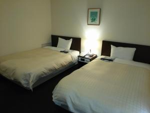 two beds in a hotel room with a lamp on a table at Hirosaki Grand Hotel in Hirosaki