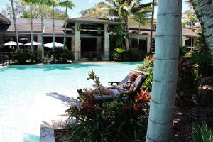 a woman sitting in a chair next to a swimming pool at 132 Temple Luxury Direct Studio in Port Douglas