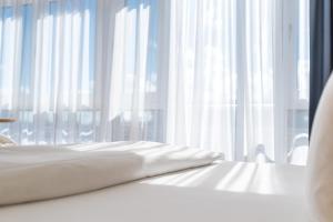 a white bed with white curtains in front of a window at Strand-Hotel Hübner in Warnemünde