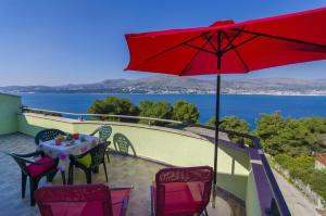a table and chairs on a balcony with a red umbrella at Apartments Pava in Okrug Donji
