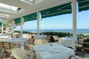 um restaurante com mesas e cadeiras brancas e o oceano em Hotel Beau Sejour em Alassio
