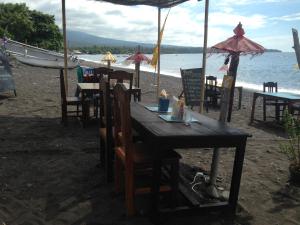 a wooden table on the beach with chairs and umbrellas at Homestay & Restaurant Segara Amed in Amed