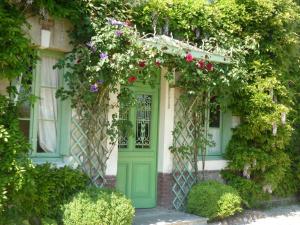 uma entrada para uma casa com uma porta verde e flores em Le Clos des ifs em Thiétreville