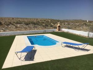 a swimming pool with two blue chairs on a lawn at Cuevas del Cipres in Baza