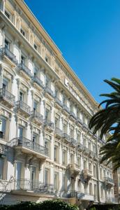 a large white building with balconies and a palm tree at Hôtel West End Promenade in Nice