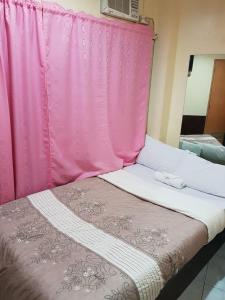 a bed with a pink curtain next to a window at City Corner Hotel in Legazpi