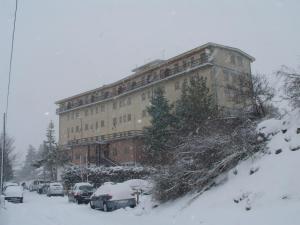 un grand bâtiment avec des voitures garées dans la neige dans l'établissement Hotel Caldora, à Rocca di Mezzo