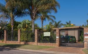 a brick fence with a gate with palm trees at Rest-a-While Guest House - Pretoria in Pretoria