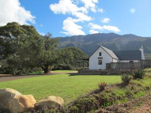 une grange blanche dans un champ avec des montagnes en arrière-plan dans l'établissement Die Ou Huis Accommodation, à Ashton