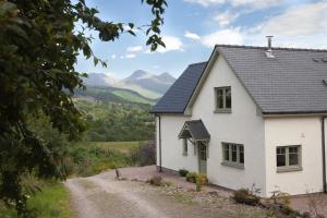 a white house on a dirt road with mountains in the background at Bluebell Croft in Strontian