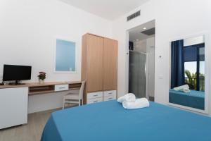 sypialnia z niebieskim łóżkiem, biurkiem i telewizorem w obiekcie Ticho's Greenblu Hotel w mieście Castellaneta Marina