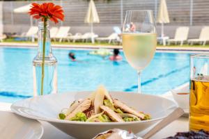 un piatto di cibo e un bicchiere di vino accanto a una piscina di Dimitra & Evdokia Hotel ad Agia Marina Nea Kydonias
