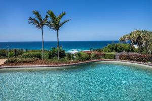 a swimming pool with palm trees and the ocean at Sunseeker Holiday Apartments in Sunshine Beach