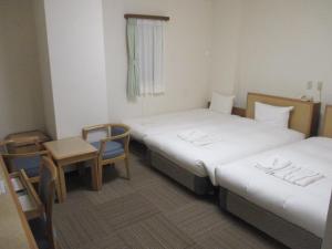 two beds in a small room with a table and chairs at Hotel Green Well in Sendai