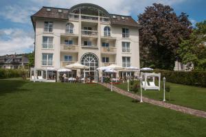 un grand bâtiment avec des parasols en face de celui-ci dans l'établissement Villa Christina, à Pörtschach am Wörthersee