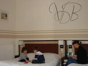 Logis Hotels Restaurants- Villa des Bordes في Cléry-Saint-André: امرأة وطفلين جالسين على سرير
