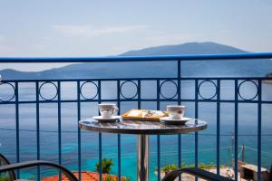 a table with two cups and a book on a balcony at Olive Bay Hotel in Ayia Evfimia