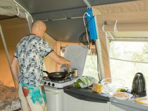 un hombre cocinando en una estufa en una caravana en Country Camp camping Nommerlayen en Nommern