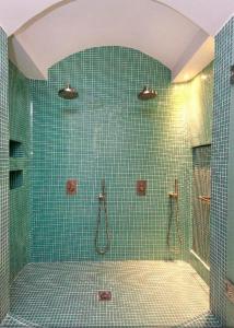 baño de azulejos verdes con ducha y puerta de cristal en Allure Suites, en Firostefani