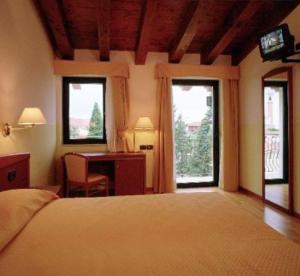 a bedroom with a bed and a desk and two windows at Hotel Ristorante Pedrocchi in San Giorgio di Perlena