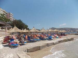 um grupo de pessoas sentadas numa praia com guarda-sóis em Hotel Piccolino em Sarandë